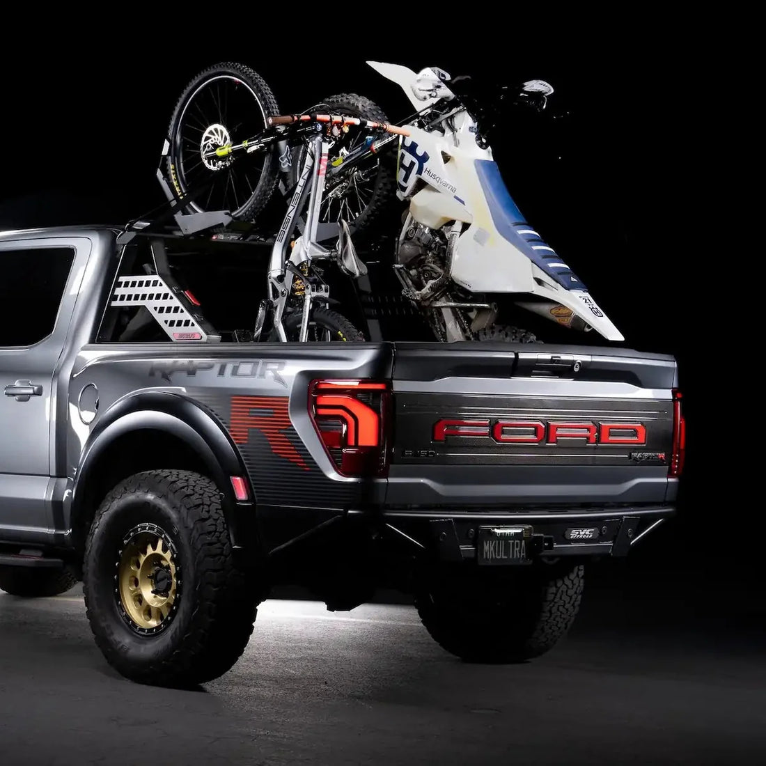 Ford Raptor truck with a bike and motorcycle in the bed on a black background