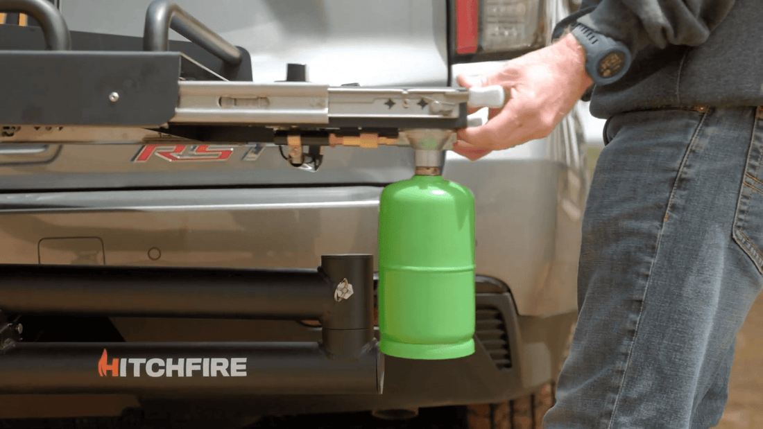 Person attaching a green propane tank to a HitchFire device on a vehicle