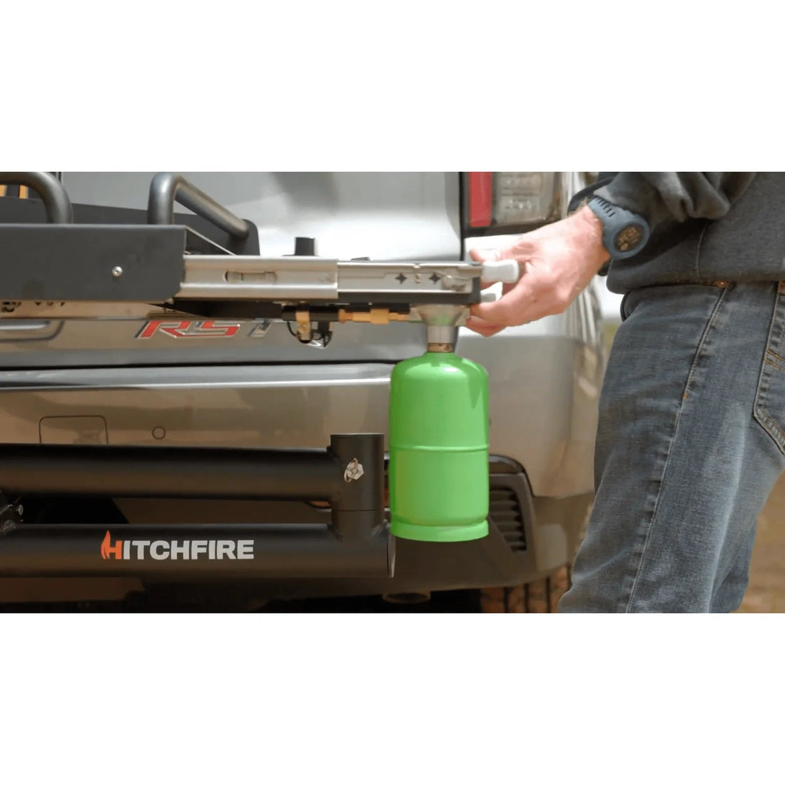 Person attaching a green propane tank to a HitchFire device on a vehicle