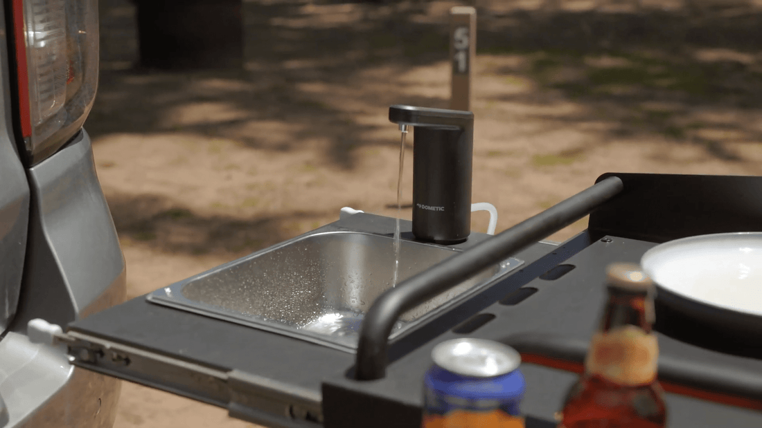 Portable outdoor kitchen sink with water flowing, surrounded by bottles on a natural background.