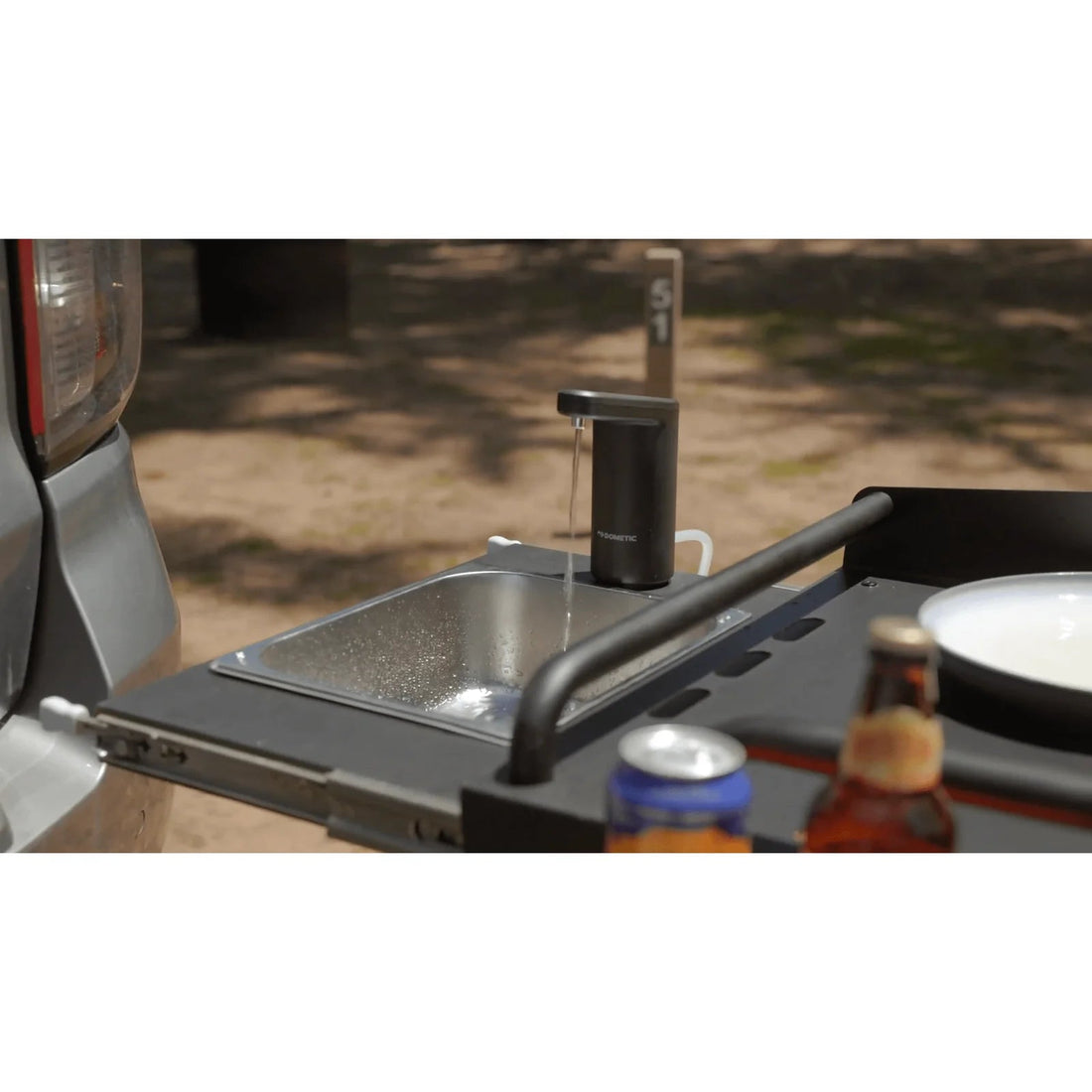 Portable outdoor kitchen sink with water flowing, surrounded by bottles on a natural background.