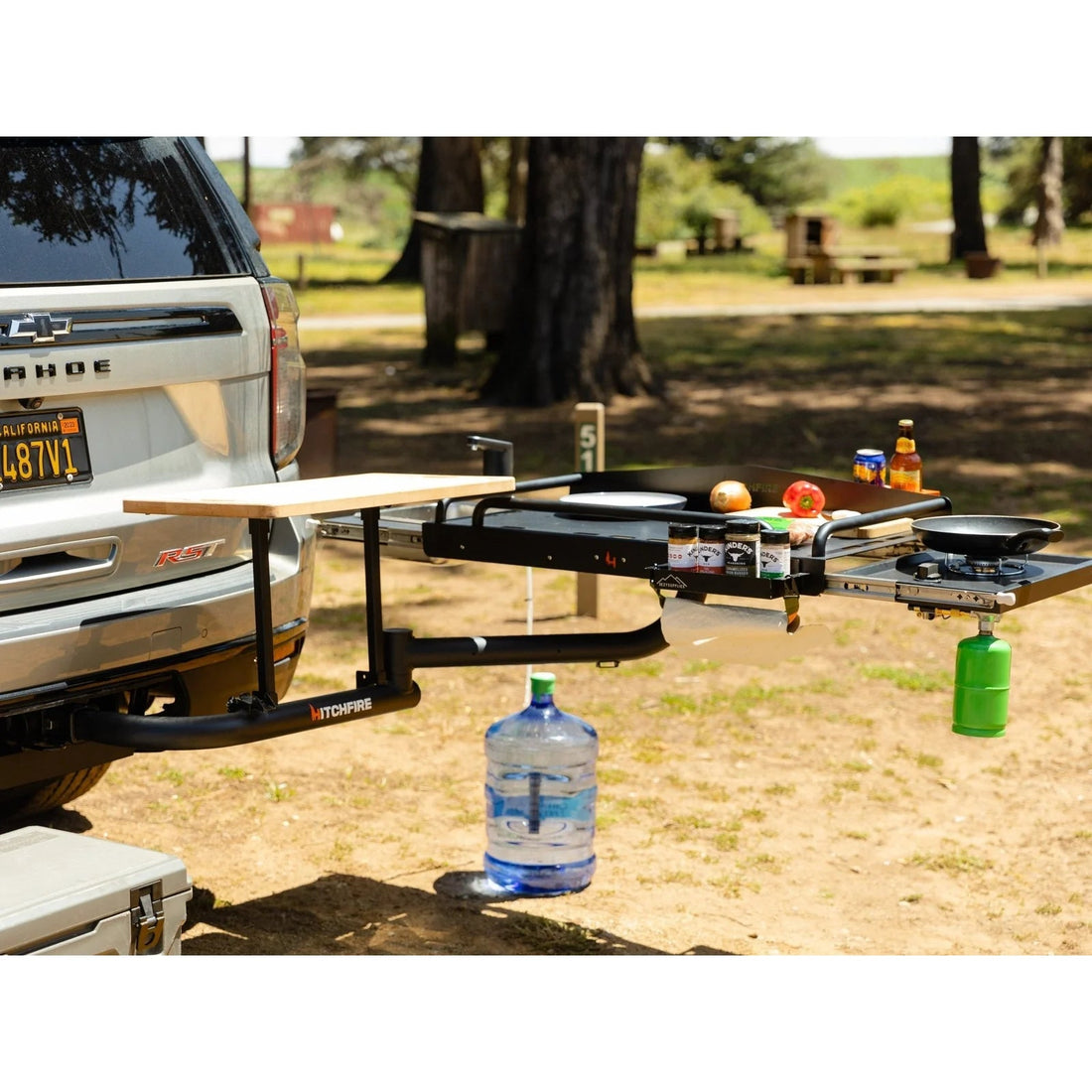 Outdoor setting with a truck tailgate extension featuring a portable stove and cooking items.