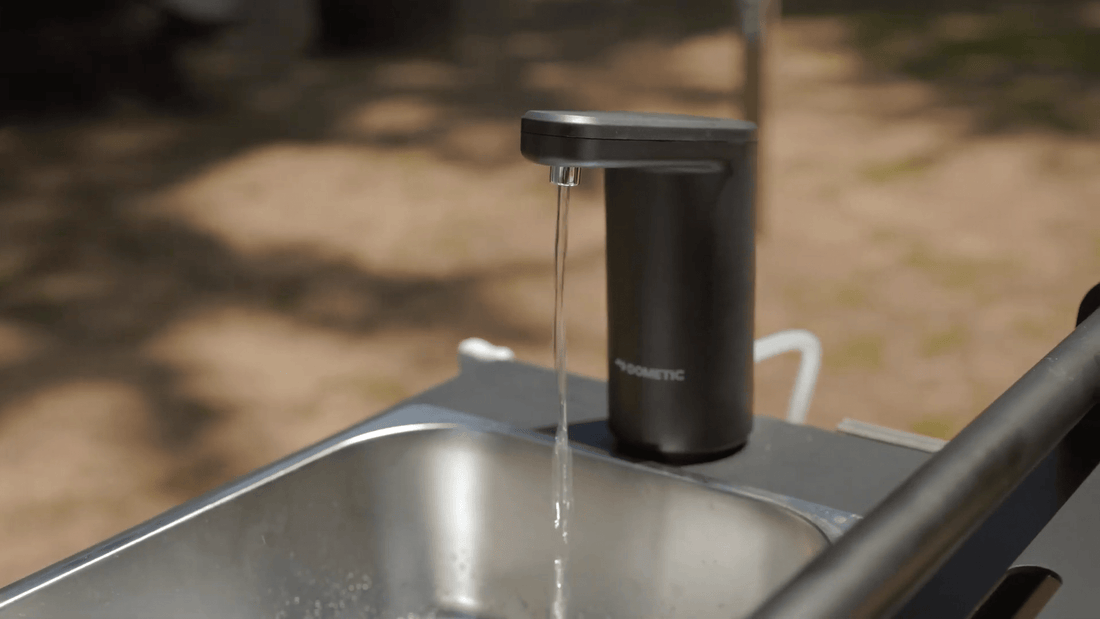 Black soap dispenser on a sink with water flowing, outdoor setting