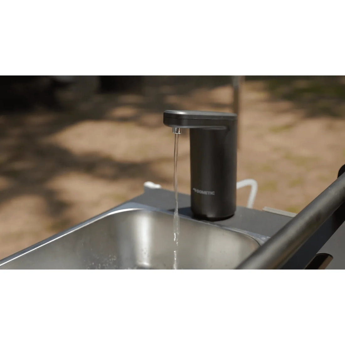 Black soap dispenser on a sink with water flowing, outdoor setting