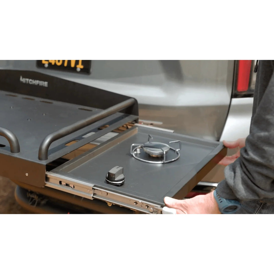 Portable stove top with a person holding it next to a vehicle