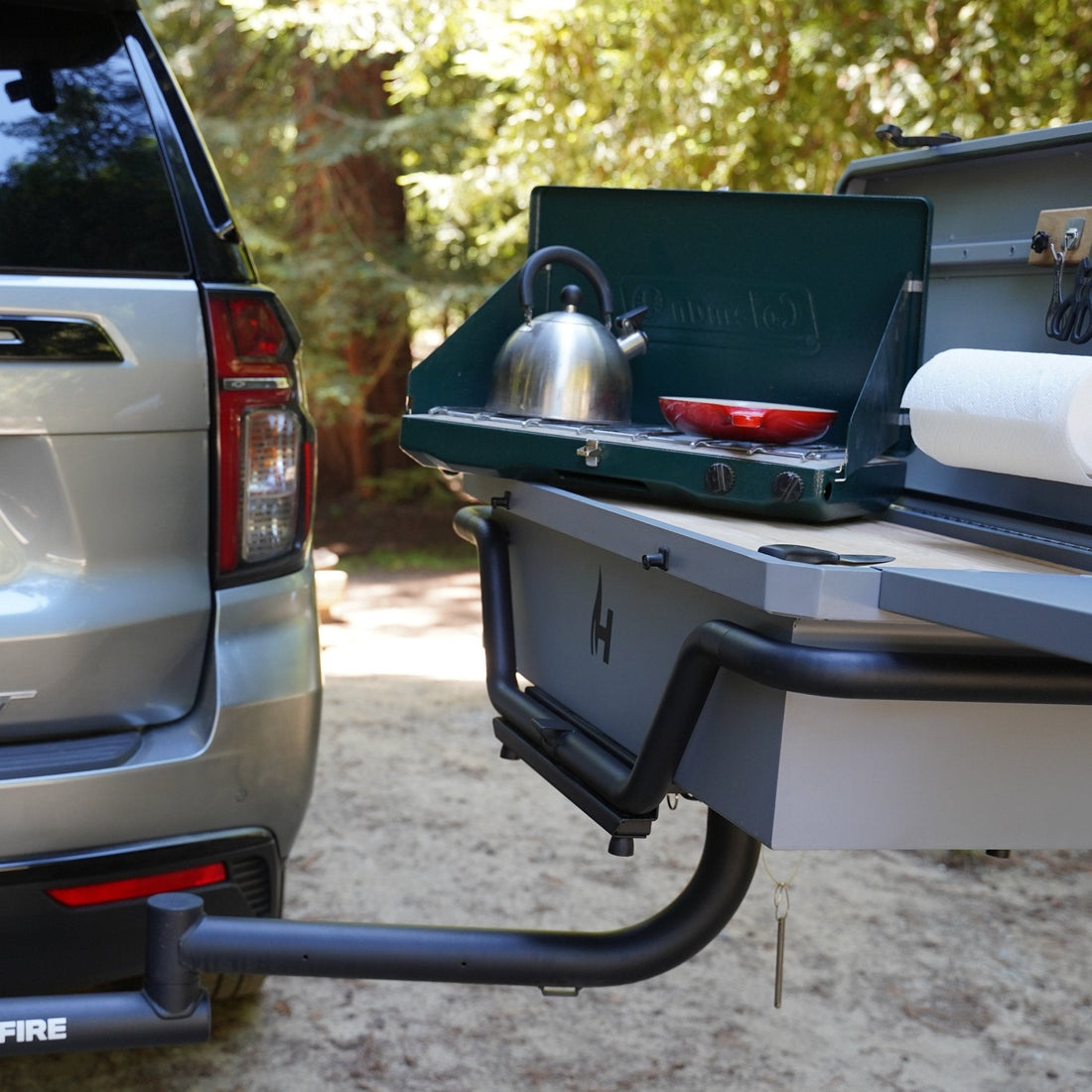 Portable outdoor kitchen attached to a vehicle with a kettle and pot on a sunny day.