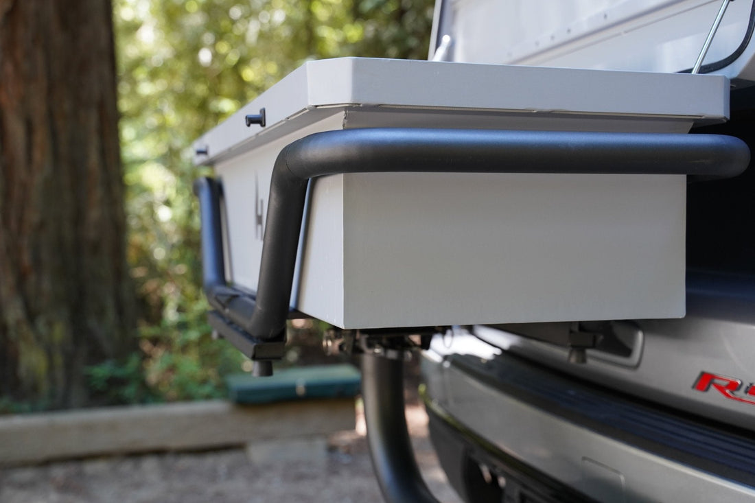 Back of a vehicle with a roof rack and storage box, outdoors.