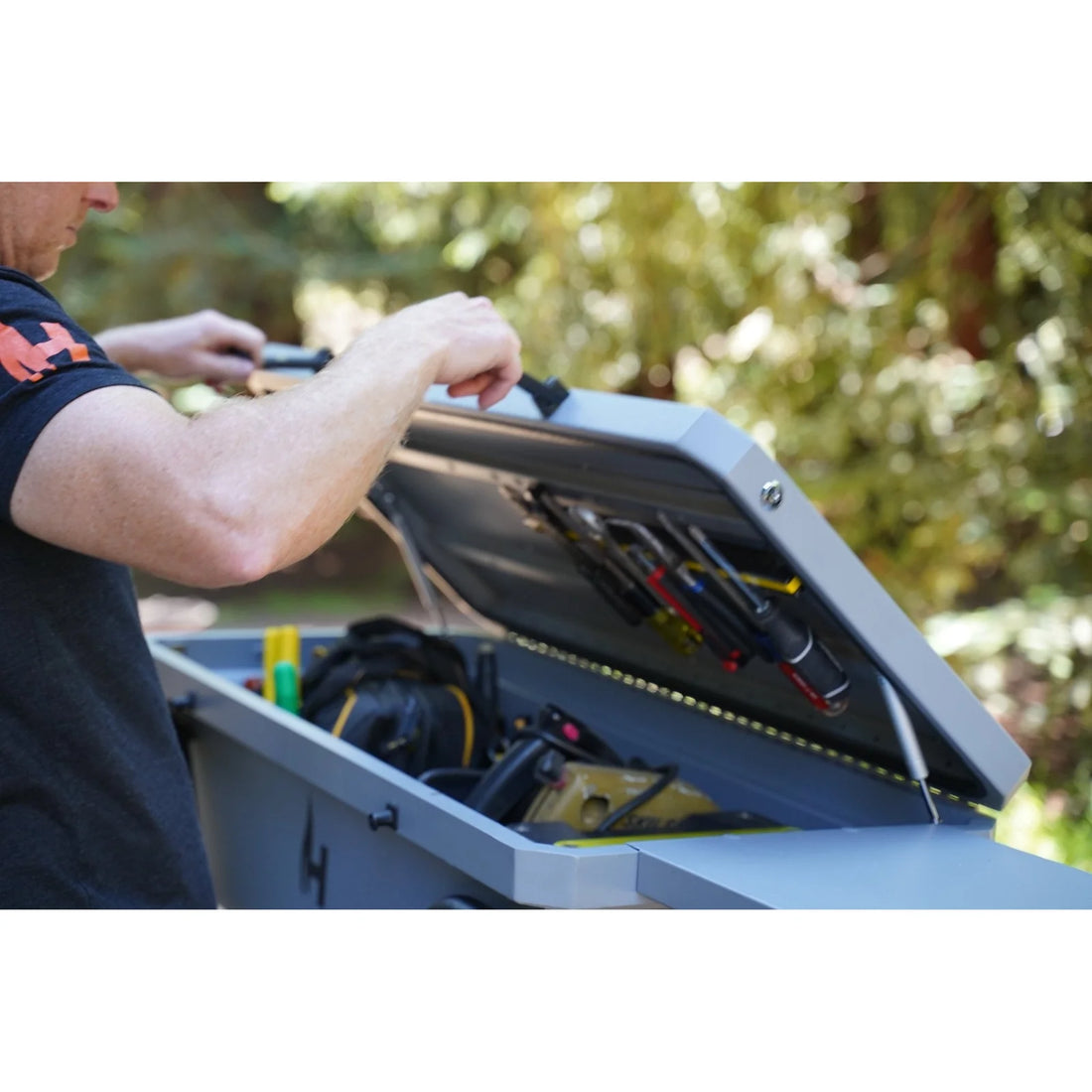 Person opening a tool box with tools inside, outdoors.