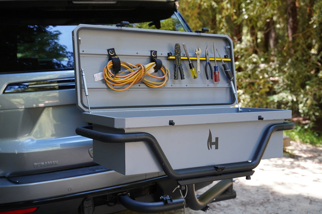 Tool box attached to a vehicle with tools and cables inside, outdoors.