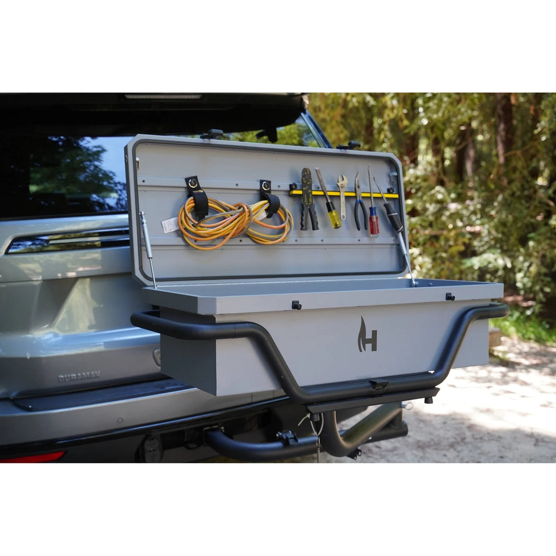 Tool box attached to a vehicle with tools and cables inside, outdoors.