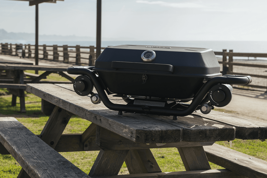 Portable grill on a wooden picnic table with a scenic background