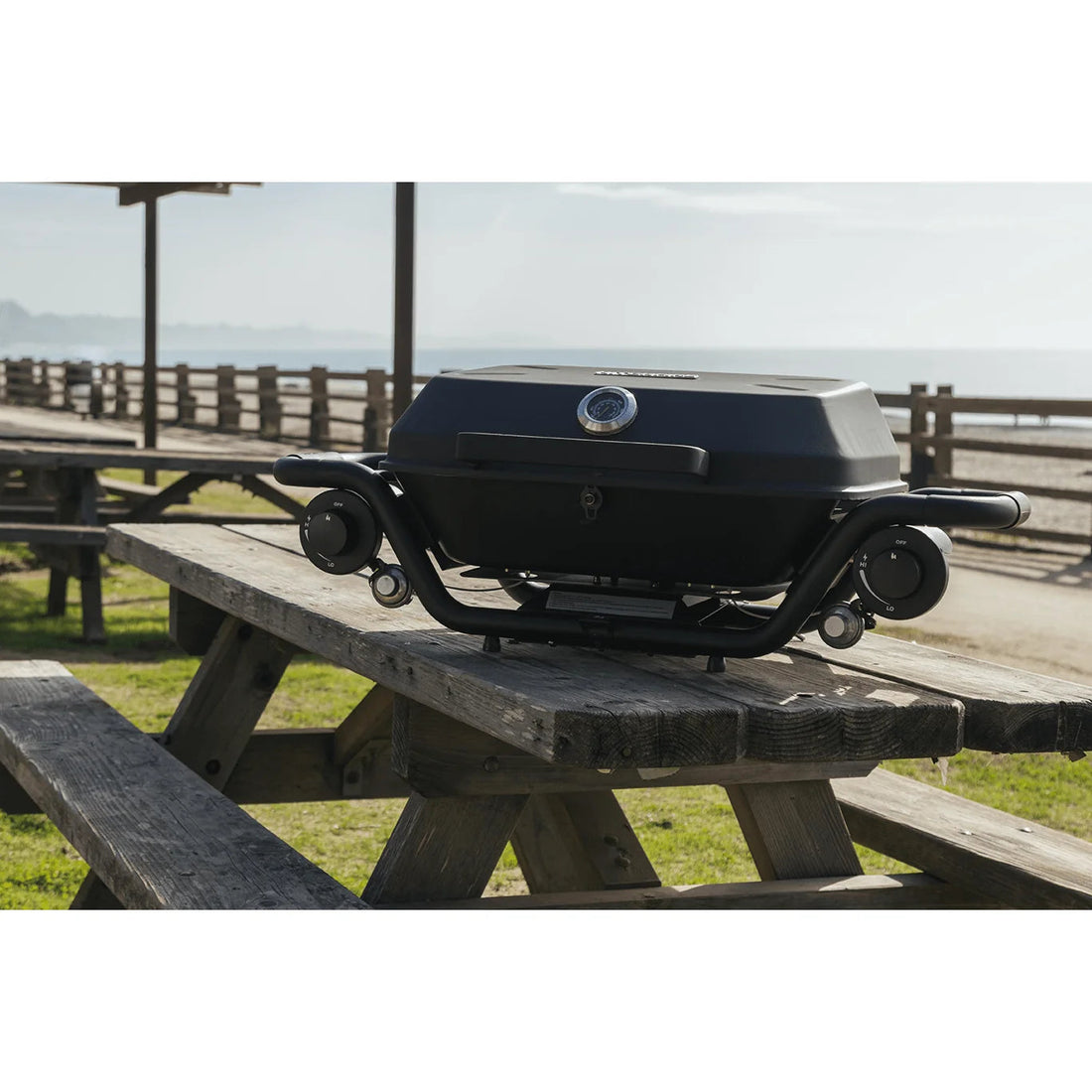 Portable grill on a wooden picnic table with a scenic background
