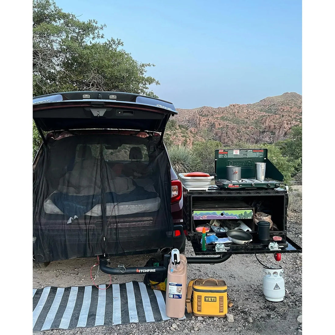 HitchFire swing arm setup behind an open SUV tailgate at camp