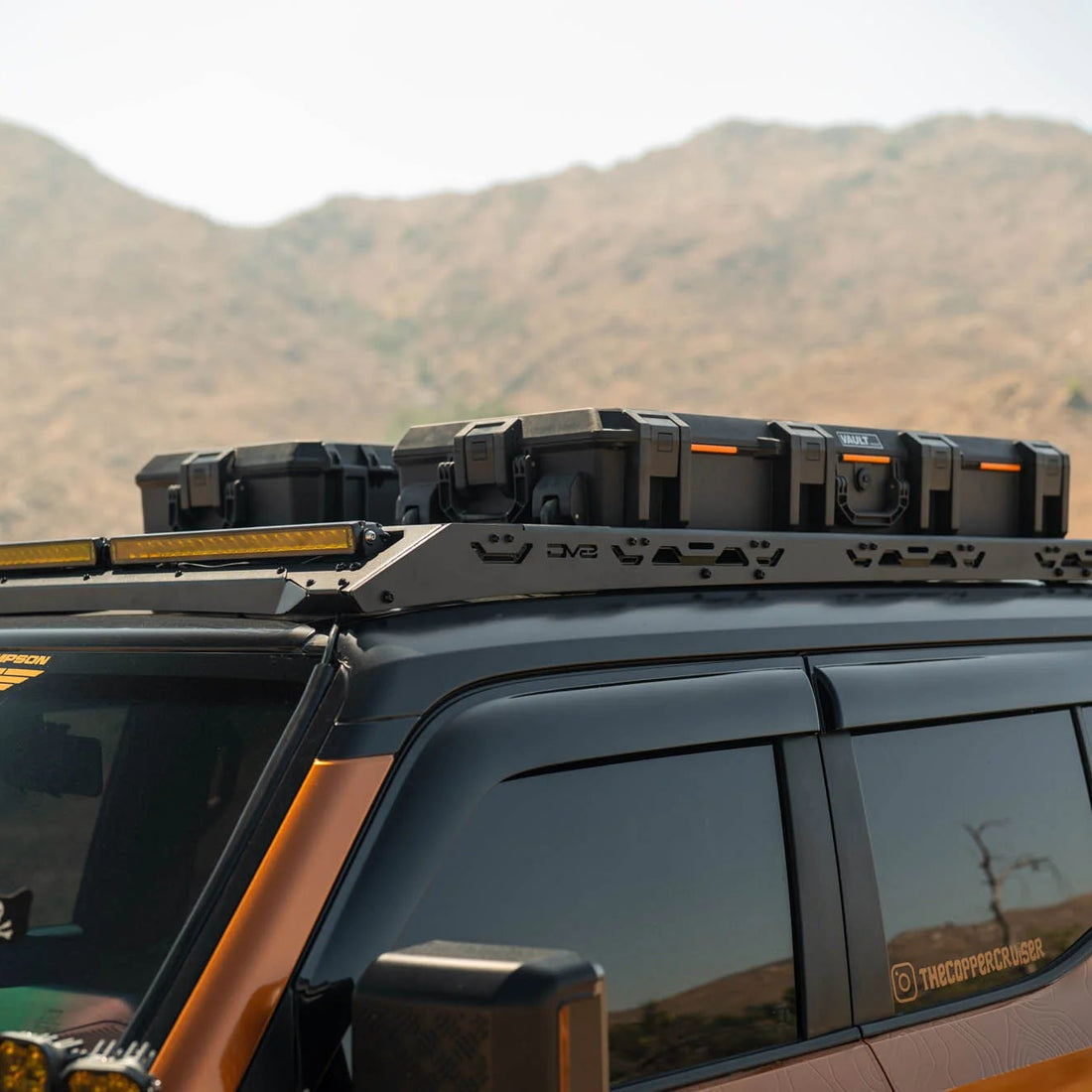 SUV with roof rack and off-road lights against a mountainous landscape