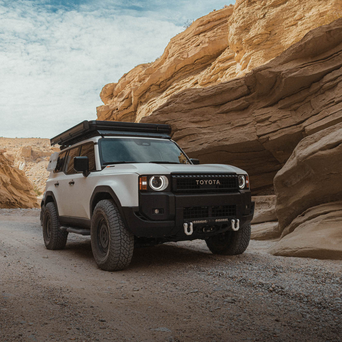 White Toyota SUV with roof rack in a desert canyon