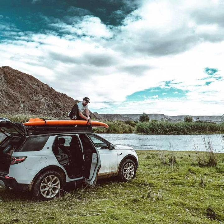 Front Runner Pro Canoe / Kayak / SUP Carrier holding a kayak on a roof rack by a river