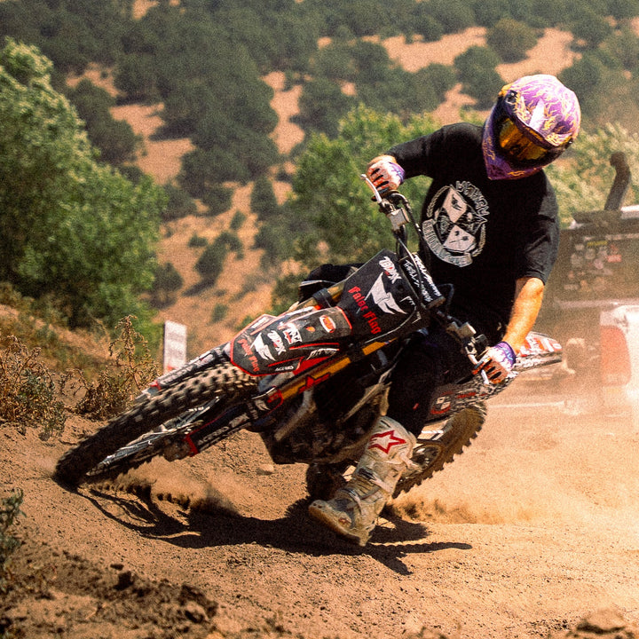 Person riding a dirt bike on a dirt road with a truck in the background