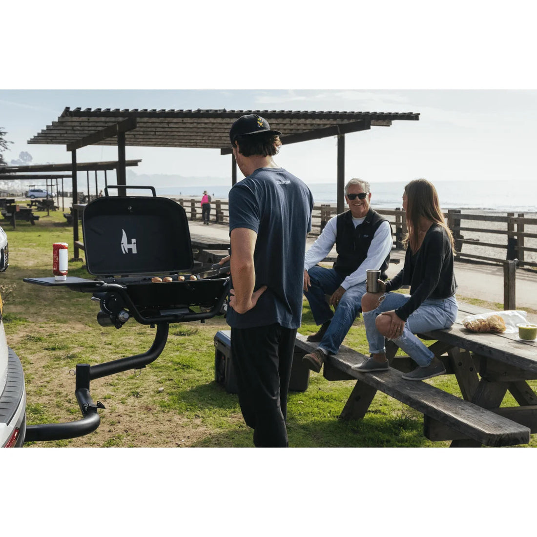 People gathered around a grill at a picnic area with a scenic background