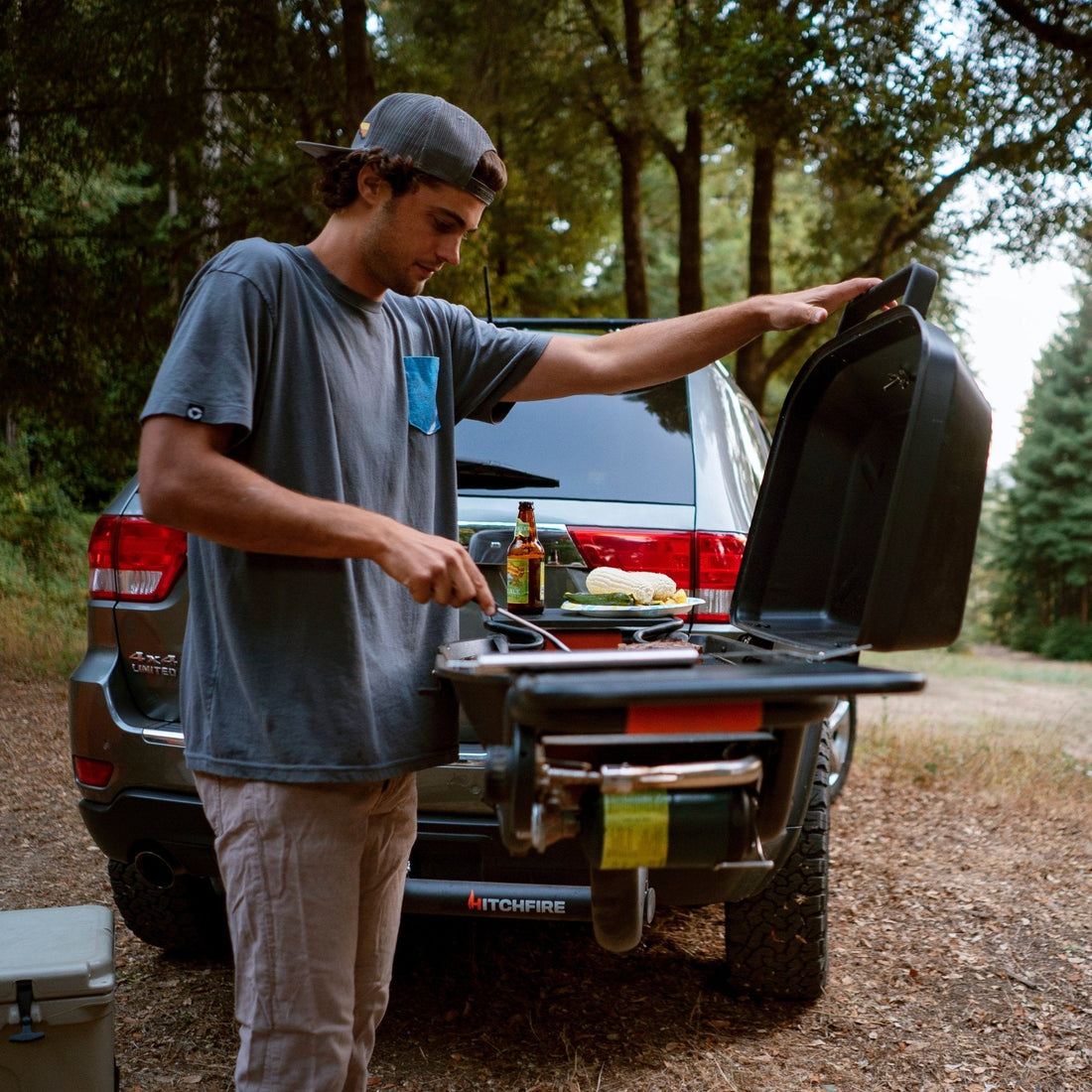 Man preparing food on a portable stove in the back of a truck outdoors.