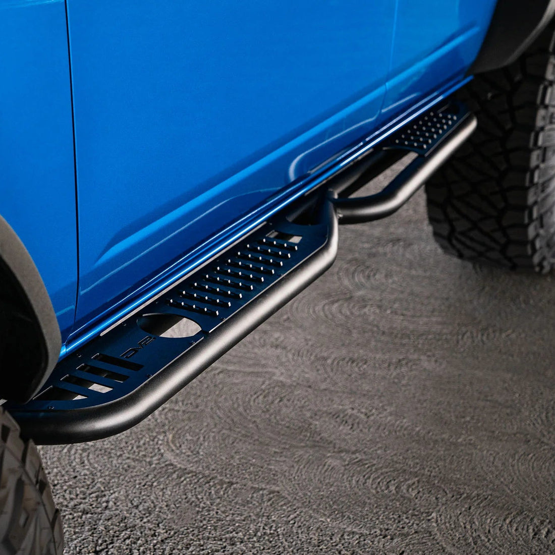 Close-up of a blue vehicle with a black side step on a textured surface