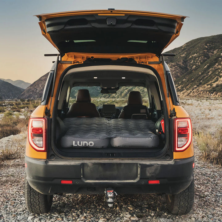 SUV with trunk open, Luno inflatable mattress setup for car camping in a mountain landscape
